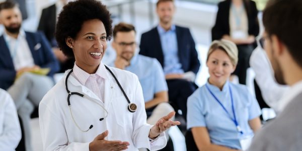 Happy African American female doctor talking to a businessman who is holding a seminar in convention hall.